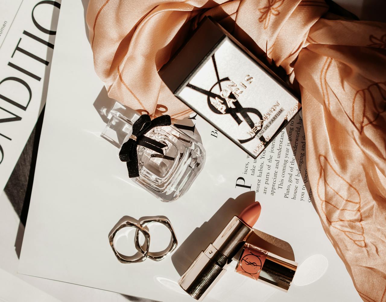 Home Sophisticated flat lay featuring luxury beauty products, including perfume and lipstick, with a stylish scarf.